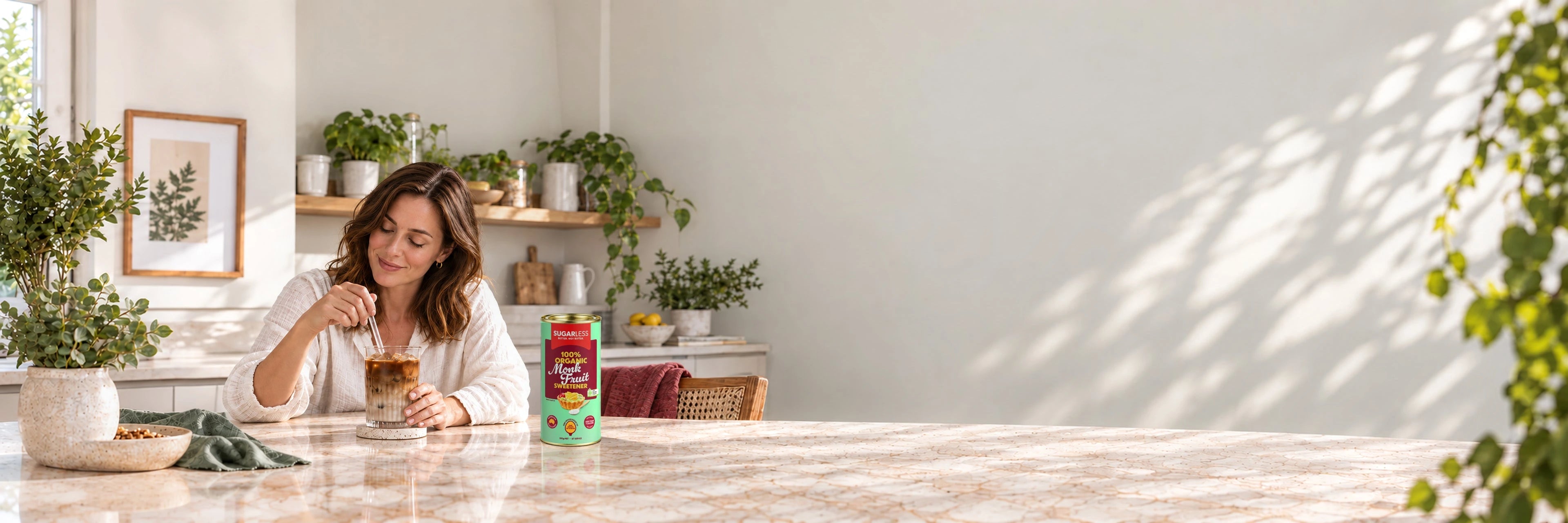 Sugarless Organic Monk Fruit 350g on a stone kitchen bench beside a woman enjoying iced coffee