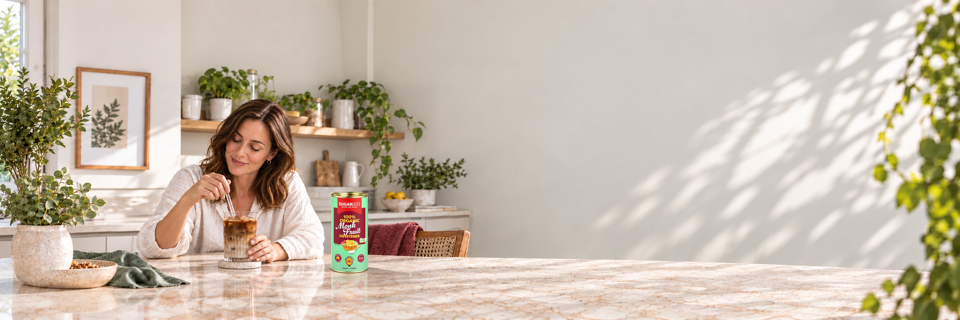 Sugarless Organic Monk Fruit 350g on a stone kitchen bench beside a woman enjoying iced coffee