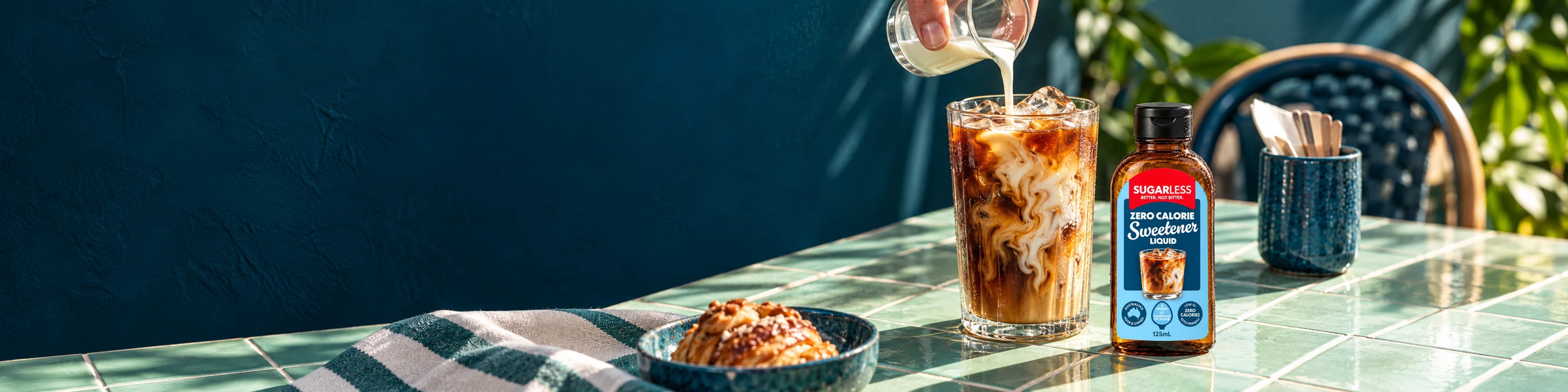 Sugarless 125 ml liquid sweetener beside iced coffee with milk being poured.